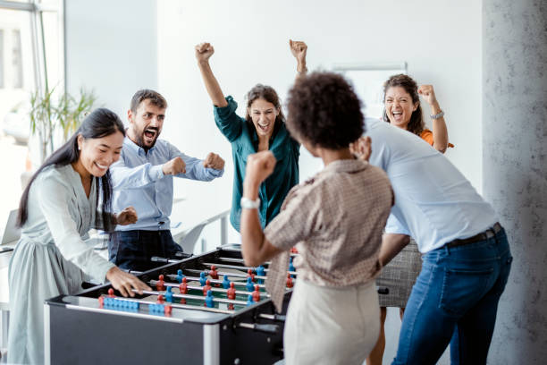 Happy multicultural business colleagues playing table football together in the office
