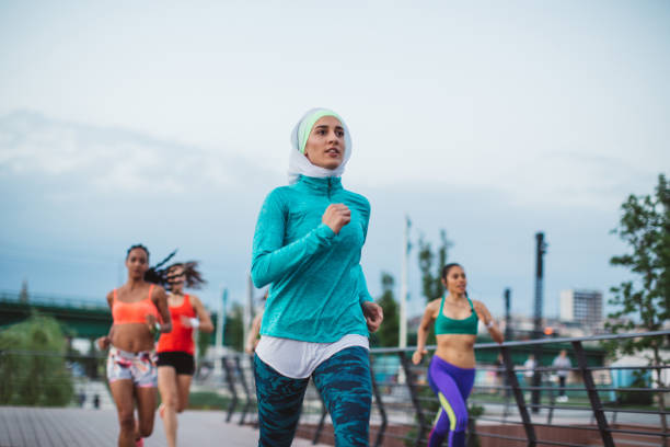 Multi ethnic group of young  women exercise outdoor, next to the river. They are wearing sport clothing, running, stretching, celebrate and support each other.